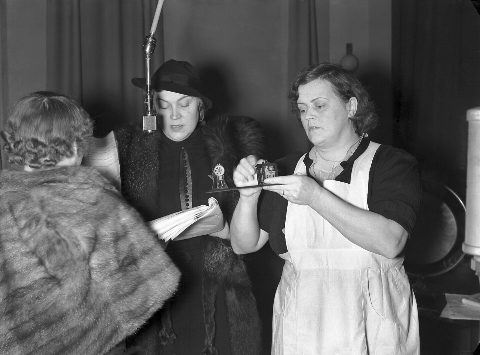 Two actresses recording a radio play at a hanging microphone in the 1930s, one reading from a script.